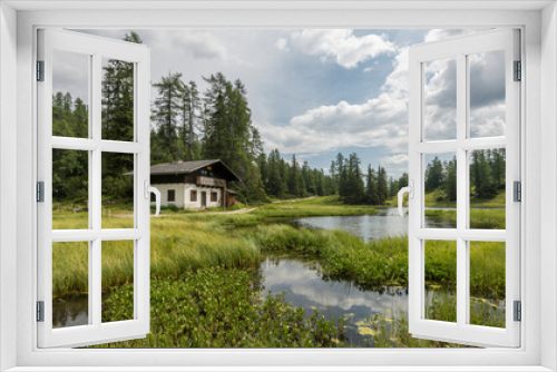 Fototapeta Naklejka Na Ścianę Okno 3D - Beautiful alpine summer view with an Austrian mountain hut on the shores of a smal lake in the Alps. Surrounded by pine trees and waterplants. water in the foreground. Travel, hike, hiking, trekking