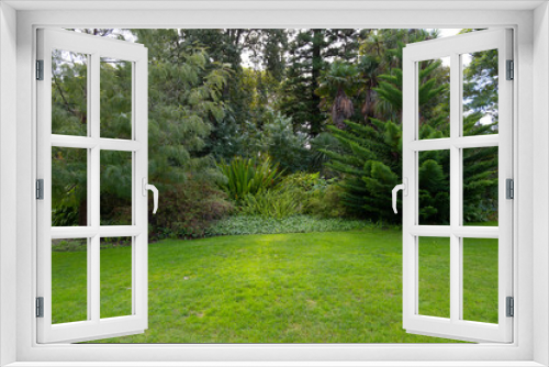 Fototapeta Naklejka Na Ścianę Okno 3D - View of green grass lawn in a formal garden with various trees and flower beds. Background texture of a grass and plants in a park or a campground. Copy space for text.