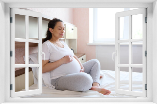 Expectant mother in last stages of pregnancy putting her hands palms on her pregnant abdomen, resting at home. Maternity