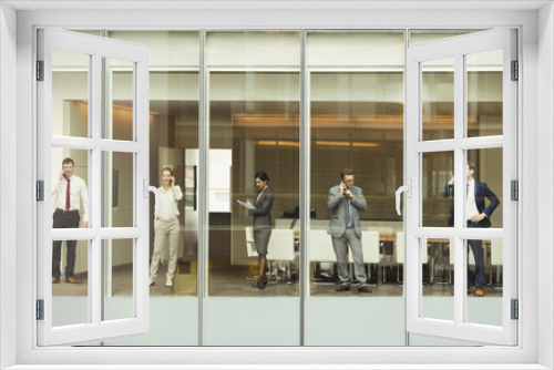 Business people talking on cell phones reviewing paperwork at conference room window