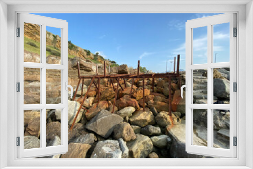 Fototapeta Naklejka Na Ścianę Okno 3D - An abandoned rusty pier platform on the cliffs by the sea. Rusty steel beams, remnants of old sea pier