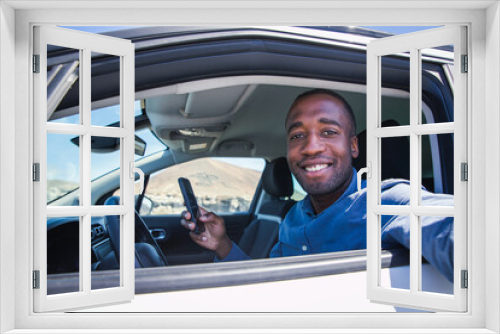 A smiling businessman sitting in his car takes a selfie while using his smartphone