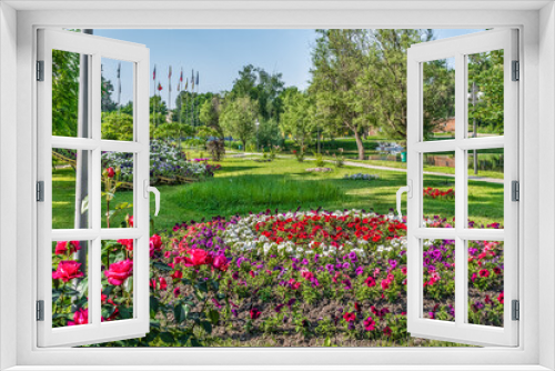 Fototapeta Naklejka Na Ścianę Okno 3D - Flowerbeds with bright pink-purple-red-white flowers among the green lawn on the lake in the Trostyanets central park, Sumy region, Ukraine. Beautiful fresh summer landscape and city garden