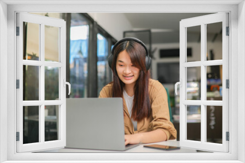 Asian woman wearing brown shirt sitting and listening to music on headphones and use a notebook computer