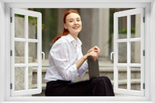 Motivated and ambitious young woman, office manager sitting on stairs outdoors and working on laptop. Deadlines