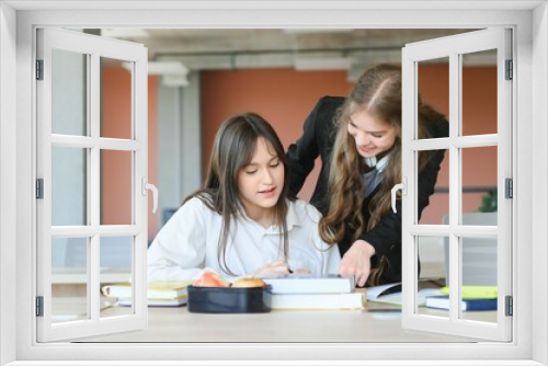 Smiling schoolgirls are talking about homework at the desk in the class.