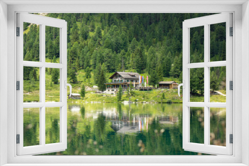 Fototapeta Naklejka Na Ścianę Okno 3D - Österreichisch aussehendes Haus an einem klaren See mit einer Spiegelung im Wasser. Bäume im Hintergrund.