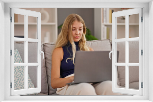 Young blonde woman using laptop sitting on sofa at home