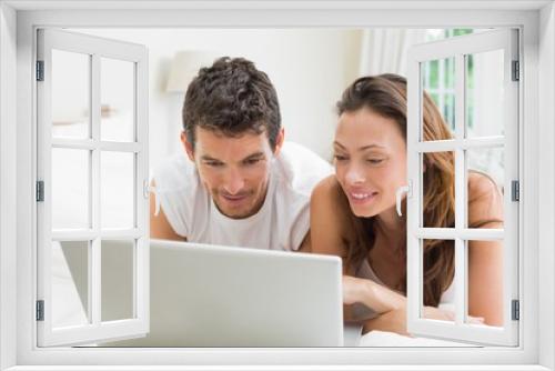 Smiling couple using laptop in bed