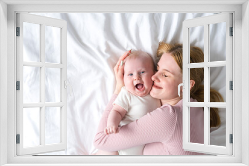 young mother hugging her baby lying on bed. top view