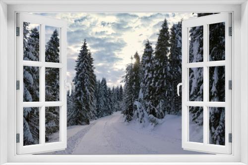 Fototapeta Naklejka Na Ścianę Okno 3D - Coniferous forest covered with snow, sunset sky with clouds in the background. Road in deep snow.