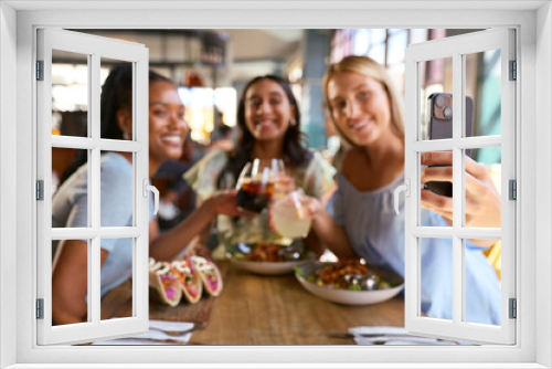 Group Of Female Friends Meeting Up In Restaurant Posing For Selfie On Mobile Phone With Food