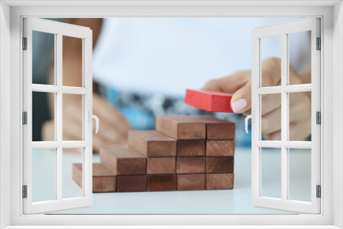 Fototapeta Naklejka Na Ścianę Okno 3D - Female hand builds ladder from wooden blocks from above red. Building successful business and career concept