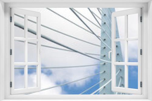 Fototapeta Naklejka Na Ścianę Okno 3D - Rotterdam, the Netherlands-February 2023; Vertical view of the top of the Erasmus suspension bridge over the Maas river with the cables against a white clouded blue sky