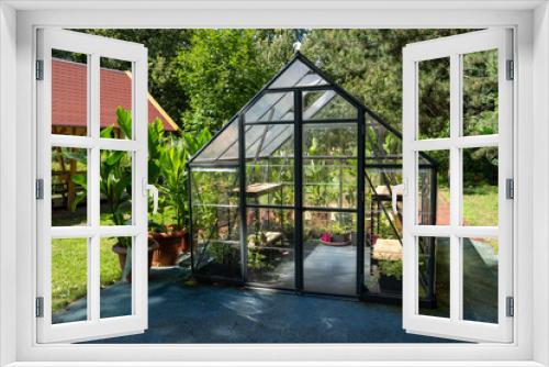 Fototapeta Naklejka Na Ścianę Okno 3D - Greenhouse in the garden. Glass small compact greenhouse for growing flowers, vegetables, seedlings of various plants. Gardening. Beautiful glass building house in yard. Hobby no dig.