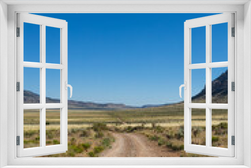 Fototapeta Naklejka Na Ścianę Okno 3D - A dirt road stretching across a vast arid valley in northern Arizona with a clear blue sky.