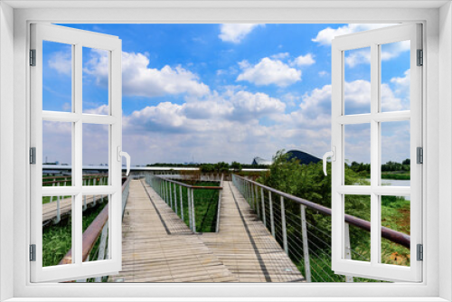 Fototapeta Naklejka Na Ścianę Okno 3D - Wooden walkway in the park with blue sky and white clouds. Landscape of Harbin Cultural Center Wetland Park. 