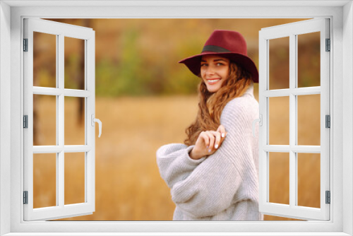 Fototapeta Naklejka Na Ścianę Okno 3D - Smiling woman in a hat in an autumn meadow enjoying the weather, spending time outdoors. Lifestyle, relaxation and weekend concept.