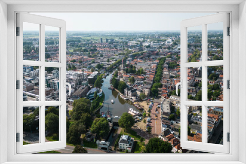 Fototapeta Naklejka Na Ścianę Okno 3D - Aerial drone shot of treetops, trees, houses and shop rooftops of Dutch city Gouda centre with historic building het Tolhuis or toll house with nieuwe veerstal road on clear sunny day