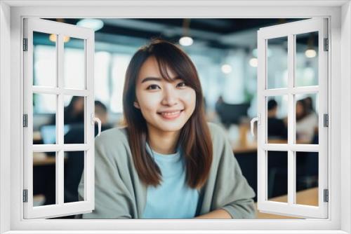 Smiling portrait of a happy young asian woman working for a modern startup company in a business office