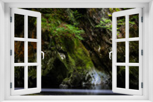Fototapeta Naklejka Na Ścianę Okno 3D - Long exposure image showing Riverside cliff with varying coloured rocks, moss, plants and the drift of water