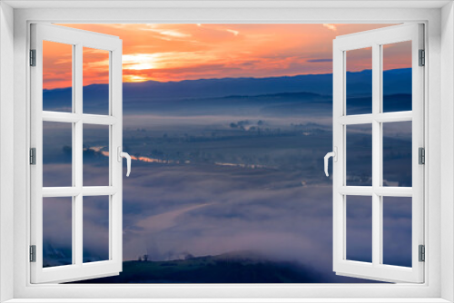 Fototapeta Naklejka Na Ścianę Okno 3D - Aerial view of the sunrise over the valley in beautiful early morning mist in the highlands. Low clouds and fog cover the sleeping meadow. Hills valley mists landscape. Serene moment in rural area