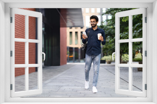Cheerful arab guy going to office, using smartphone, drinking coffee