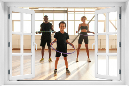 sporty african american family in sports uniform twists hula hoop and does exercises in the gym