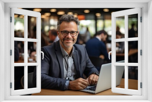 Smiling mature Indian executive in formal suit and glasses sitting at table using laptop