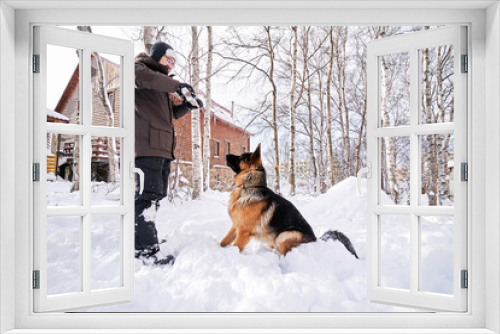 Fototapeta Naklejka Na Ścianę Okno 3D - A man plays fetch with a dog in the snowy yard of a house.