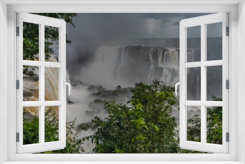 Fototapeta Naklejka Na Ścianę Okno 3D - Cascades of waterfalls fall from the ledges of rocks into the river, foaming. Spray and fog rise into the sky. Green vegetation in the foreground. Iguazu Falls. Brazil.