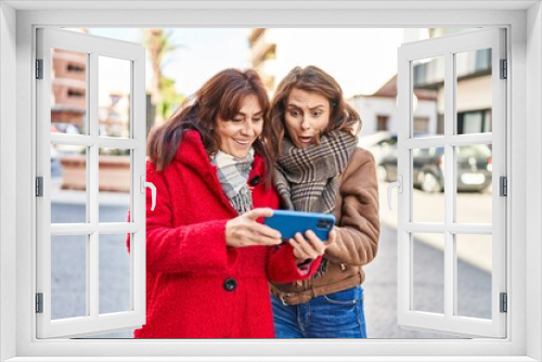 Two women mother and daughter using smartphone at street