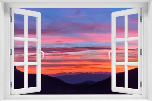 Red sunset over Passo delle Erbe with background of Dolomite peaks. Sky colored with shades of red, orange and blue, aerial view from high altitude.