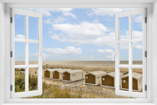 Fototapeta Naklejka Na Ścianę Okno 3D - some beach huts on the sand dunes in front of an ocean and blue sky with white puffy clouds above