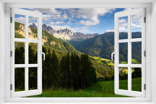 Fototapeta Naklejka Na Ścianę Okno 3D - Picture of colorful nature, forest and meadows, against background of sky and mountains, in Val de Funes region, Dolomites. In distance are lonely rural houses of local residents