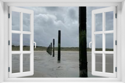 Fototapeta Naklejka Na Ścianę Okno 3D - Beach with wooden posts extending out into the waters against a cloudy sky
