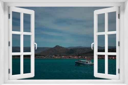 Fototapeta Naklejka Na Ścianę Okno 3D - Boat on the sea surface with green-covered hill and buildings on the background