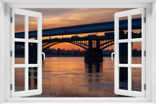 Fototapeta Naklejka Na Ścianę Okno 3D - Beautiful view of the bridge over which cars drive at sunset. A river flows under the bridge, reflecting the sunset rays. Bridge in the city of Novosibirsk, Russia
