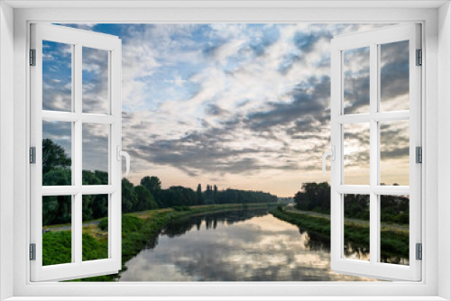 Fototapeta Naklejka Na Ścianę Okno 3D - This photograph captures the peaceful essence of a river landscape at dawn. The still waters create a perfect mirror, reflecting the awakening sky adorned with streaks of clouds. The lush riverbanks