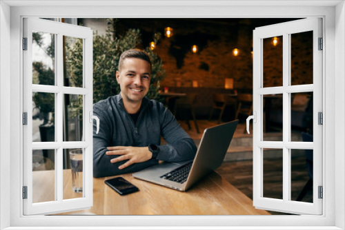 Portrait of a happy freelancer sitting in cafe with his laptop.