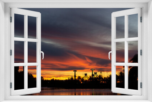 Dramatic sunset. Yellow, orange and red evening sky. Silhouettes of palm trees and park amusements