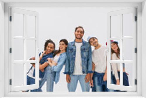 excited interracial friends posing near african american man standing with closed eyes on grey