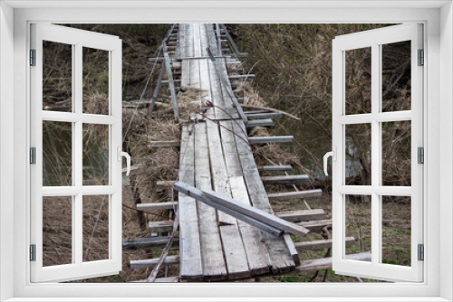 Fototapeta Naklejka Na Ścianę Okno 3D - A broken pedestrian suspension bridge in the countryside after a spring flood