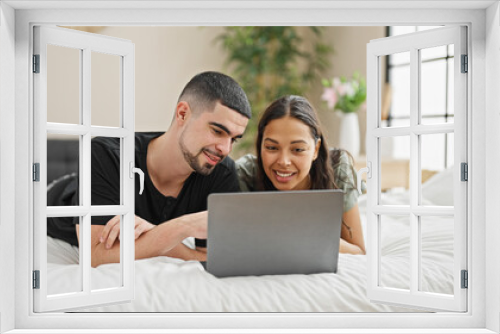 Adorable couple smiling and relaxing at home, lying in bed chatting and enjoying a lovely video call in their cosy, beautifully designed bedroom.