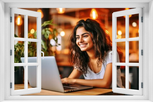 Gorgeous young lady with a happy expression using a laptop at a table in a cafe, either as a student or freelancer and gazing into the laptop