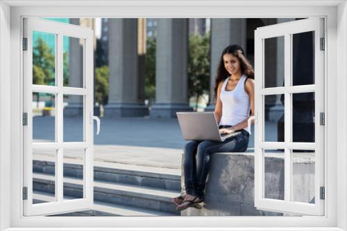 A young woman with a laptop sitting on the stairs, near the univ