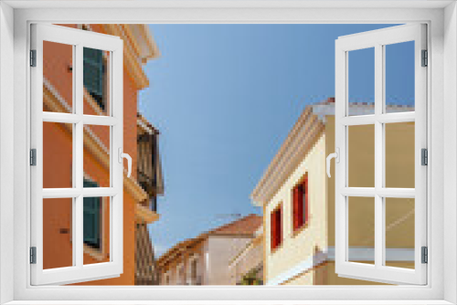 Fototapeta Naklejka Na Ścianę Okno 3D - A picturesque view of a quiet, sunlit alley framed by colorful houses with shutters, in a Mediterranean village