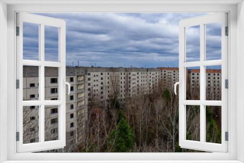 Fototapeta Naklejka Na Ścianę Okno 3D - A cloudy sky above a series of old, grey apartment buildings surrounded by bare trees.
