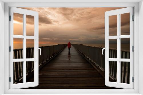 Fototapeta Naklejka Na Ścianę Okno 3D - Person walking alone on a pier enjoying dramatic sunset at the sea. Exploring nature
