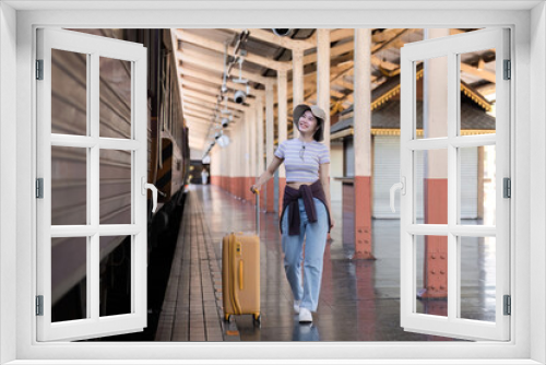 Young woman wearing an explorer's hat and carrying a suitcase Stand and look for a train at the train station. Traveler's concept